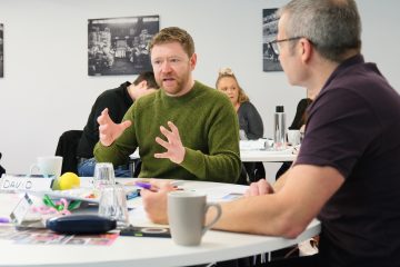 Two adult males sat at a table in discussion at a training course event